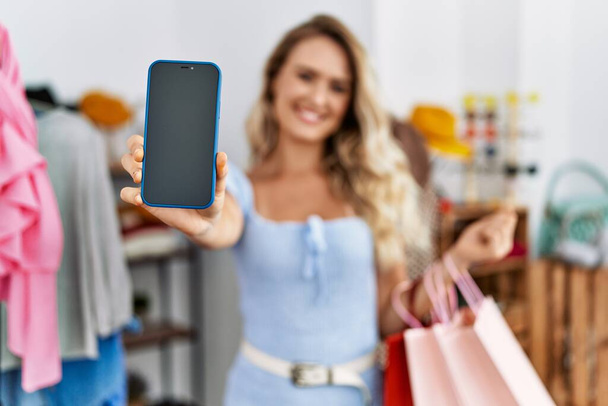 Young woman customer showing smartphone app holding shopping bags at clothing store - Photo, image