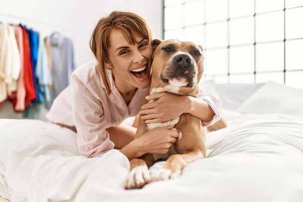 Joven mujer caucásica abrazando perro acostado en la cama en el dormitorio - Foto, Imagen