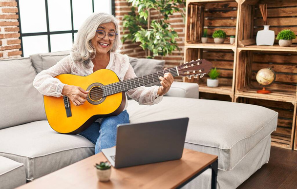 Μέση ηλικία γυναίκα που έχει online μάθημα κιθάρας στο σπίτι - Φωτογραφία, εικόνα