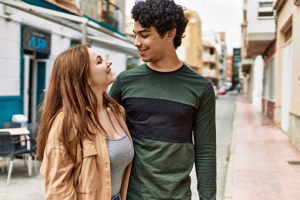 Νεαρό διαφυλετικό ζευγάρι χαμογελά χαρούμενος και αγκαλιάζει στέκεται στην πόλη. - Φωτογραφία, εικόνα