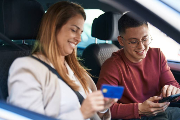 Man and woman mother and son using smartphone and credit card sitting on car at street - Foto, imagen