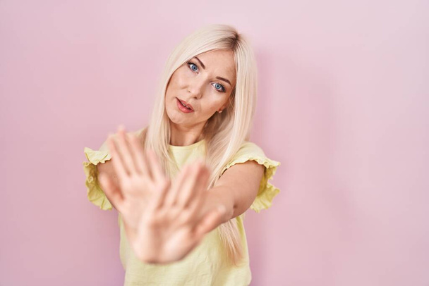ピンクの背景の拒絶表現の上に立って白人女性腕や手のひらを横断負の記号を行います,怒っている顔  - 写真・画像