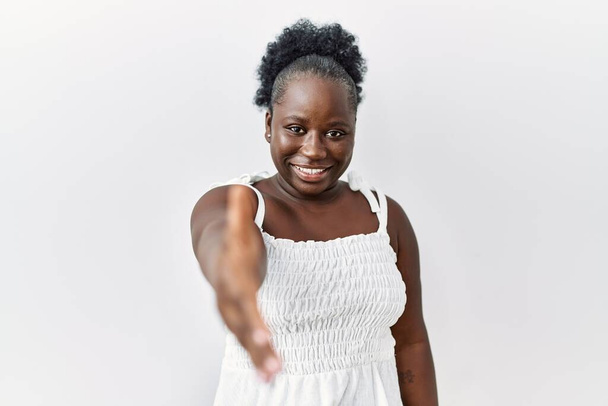 Young african woman standing over white isolated background smiling friendly offering handshake as greeting and welcoming. successful business.  - Foto, immagini