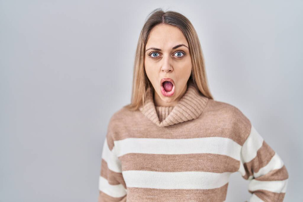 Giovane donna bionda che indossa maglione dolcevita su sfondo isolato in faccia shock, guardando scettico e sarcastico, sorpreso a bocca aperta  - Foto, immagini