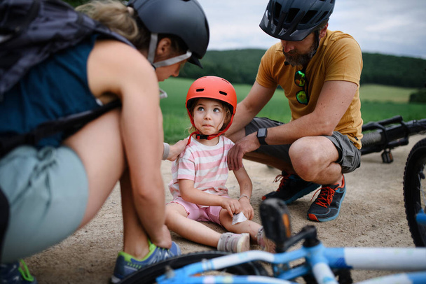 A mother and father helping their little daughter after falling off bicycle outdoors - Fotografie, Obrázek