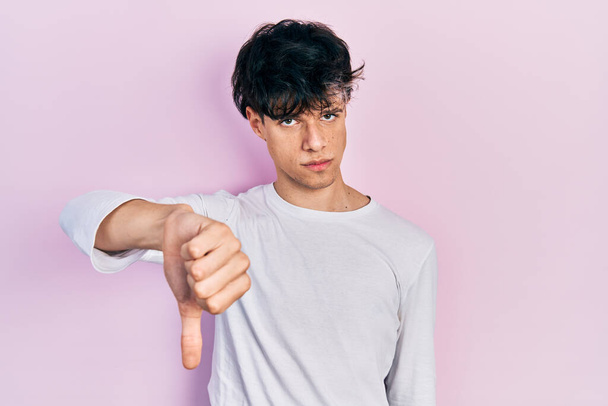 Handsome hipster young man wearing casual white shirt looking unhappy and angry showing rejection and negative with thumbs down gesture. bad expression.  - Photo, Image