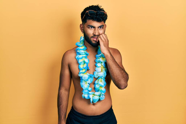 Arab man with beard wearing swimsuit and hawaiian lei looking stressed and nervous with hands on mouth biting nails. anxiety problem.  - Photo, Image