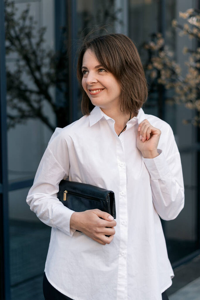 Resmi iş kıyafetleri içinde şık bir genç bayan. Resmi gömlek ve siyah debriyaj. Sıradan stil - Fotoğraf, Görsel