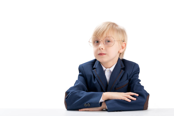 Portrait of smart blond schoolboy on white background. Elementary school student wears glasses sit idly by at desk. Fidget boy. Copy space. - Foto, imagen