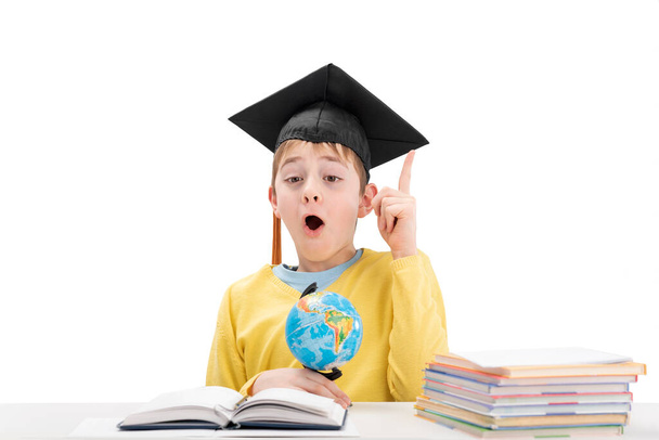 Surprised schoolboy in student hat raised index finger up. Concept idea or insight in child. Excellent student. White background. - Photo, Image