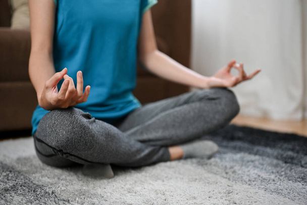 cropped image, Pleased and calm Asian woman sits on a carpet practicing a yoga lotus pose. Meditating at home - Foto, imagen