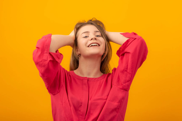 Attractive girl with hands behind head smiles and looks into the camera. Portrait of young woman on yellow background - Fotó, kép