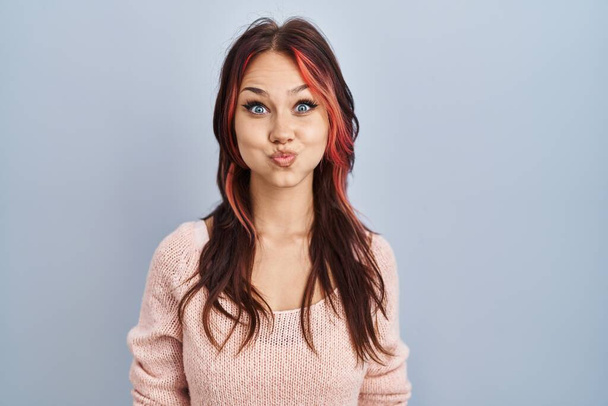 Молода біла жінка в рожевому светрі над ізольованим фоном набиває щоки смішним обличчям. рот надутий повітрям, божевільний вираз
.  - Фото, зображення