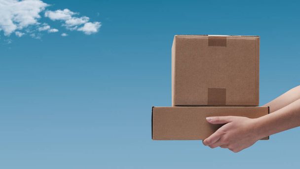 Hands holding delivery boxes and blue sky in the background: delivery and shipping concept - Foto, Imagem