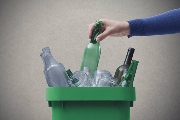 Woman putting a glass bottle in the trash bin, separate waste collection and recycling concept - Foto, afbeelding