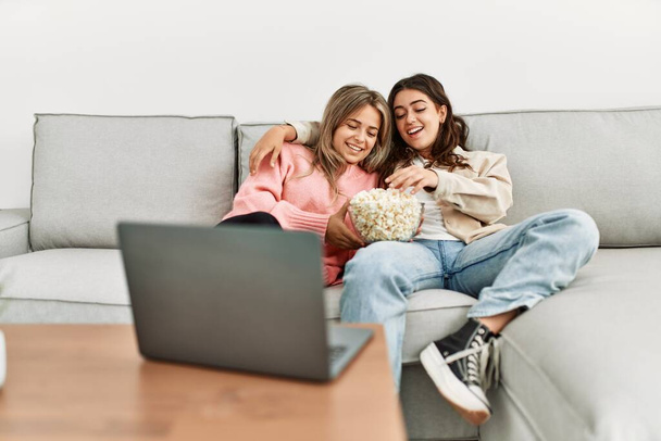 Young couple watching film and eating popcorn sitting on the sofa at home. - Foto, afbeelding