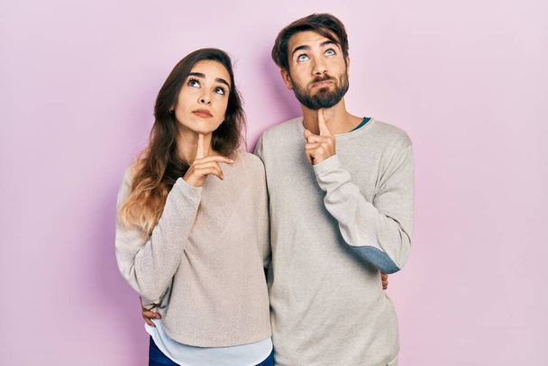 Νεαρό ζευγάρι ισπανόφωνων που φορούν καθημερινά ρούχα και σκέφτονται συγκεντρωμένα στην αμφιβολία με το δάχτυλο στο πηγούνι και αναρωτιούνται  - Φωτογραφία, εικόνα