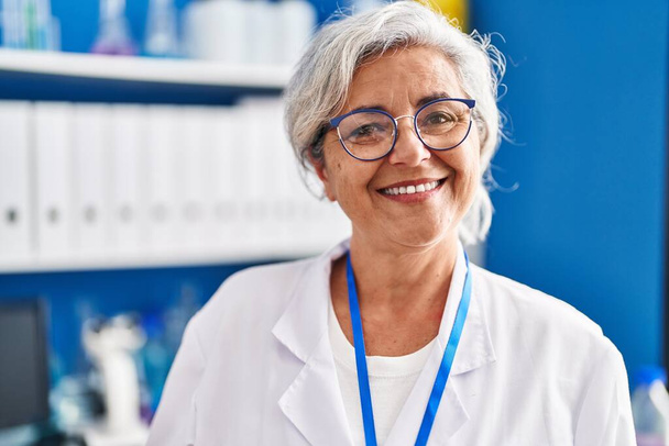 Middle age woman wearing scientist uniform standing at laboratory - Fotoğraf, Görsel
