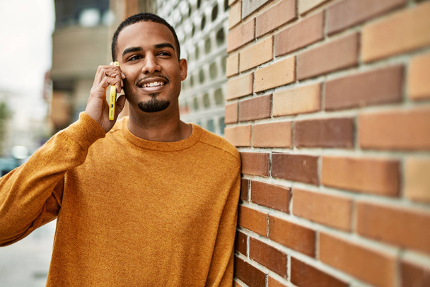 Nuori afrikkalainen amerikkalainen mies hymyilee onnellinen puhuu älypuhelimella kaupungin. - Valokuva, kuva