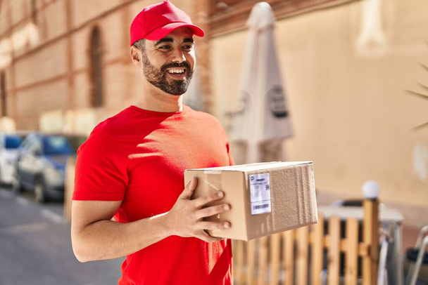 Young hispanic man courier holding package at street - Foto, imagen
