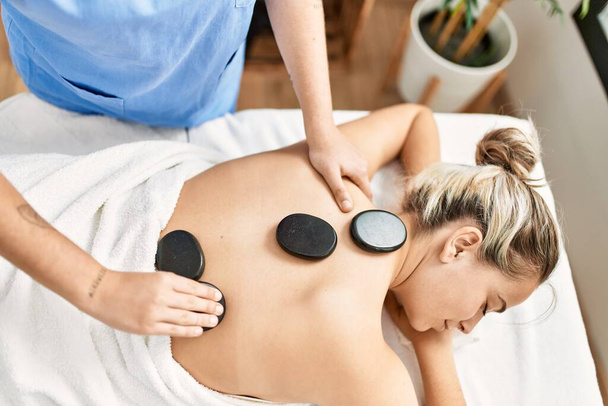 Woman couple having back treatment using hot black stones at beauty center - 写真・画像