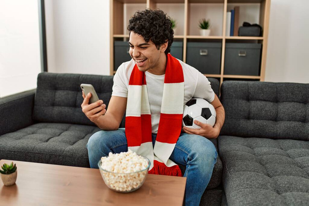 Young hispanic man watching soccer match and supporting team at home. - Photo, Image
