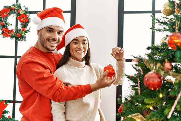 Young hispanic couple smiling happy decorating christmas tree at home. - Photo, Image