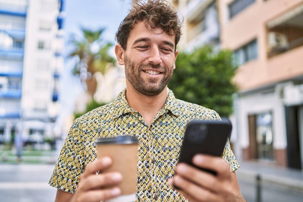 Genç İspanyol adam akıllı telefon kullanıyor, sokakta kahve içiyor. - Fotoğraf, Görsel