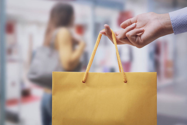Woman holding a shopping bag and stores in the background - Foto, Bild