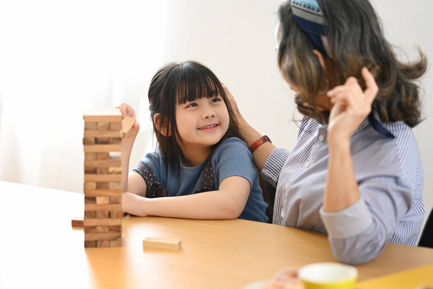 Happy mature grandma and little grandchild enjoy playing wood block stacking board game, spending leisure weekend at home together. - Photo, Image