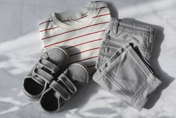 Child cloth and accessories in flat lay style. Striped t-shirt, grey jeans shorts, sneakers. Top view, flat lay - Fotó, kép