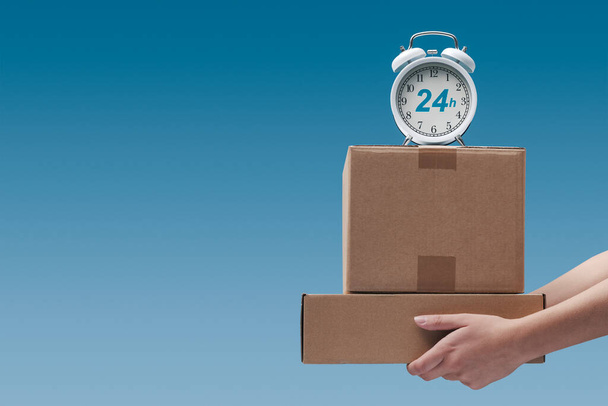 Hands holding delivery boxes and alarm clock: 24 hours delivery service, blank copy space - Photo, Image