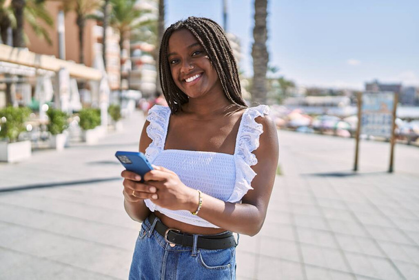 Jeune fille afro-américaine souriante heureuse en utilisant un smartphone sur la promenade. - Photo, image