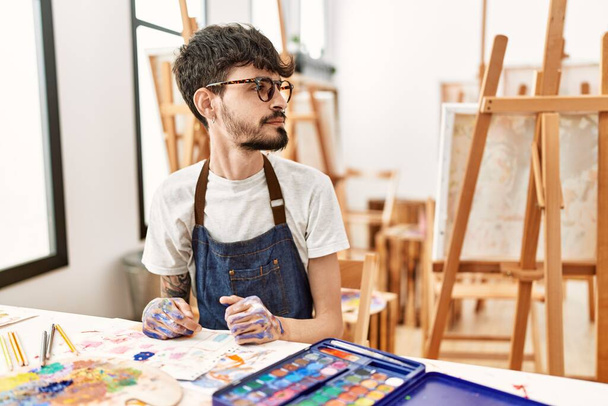 Hispanischer Mann mit Bart im Kunststudio mit Blick zur Seite, entspannte Profil-Pose mit natürlichem Gesicht und selbstbewusstem Lächeln.  - Foto, Bild