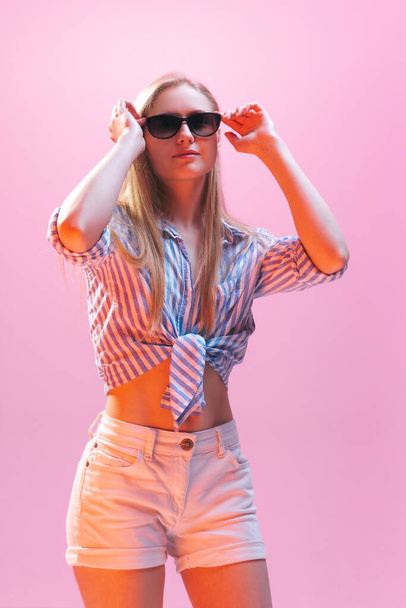 Beauty. One young beautiful girl, student wearing shirt and denim shorts isolated on pink background in neon light. Concept of human emotions, facial expression, youth, aspiration, ad - Фото, зображення