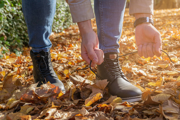 homem irreconhecível amarrando suas botas em primeiro plano contra um fundo de outono de folhas secas - Foto, Imagem