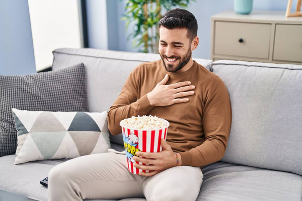 Young hispanic man watching movie sitting on sofa at home - Foto, afbeelding