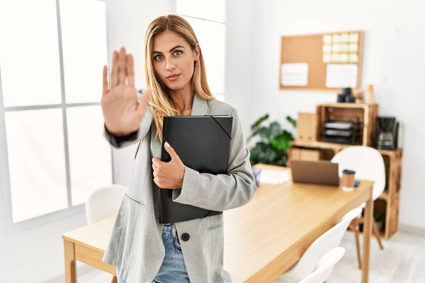 Blonde business woman at the office doing stop sing with palm of the hand. warning expression with negative and serious gesture on the face.  - Photo, Image