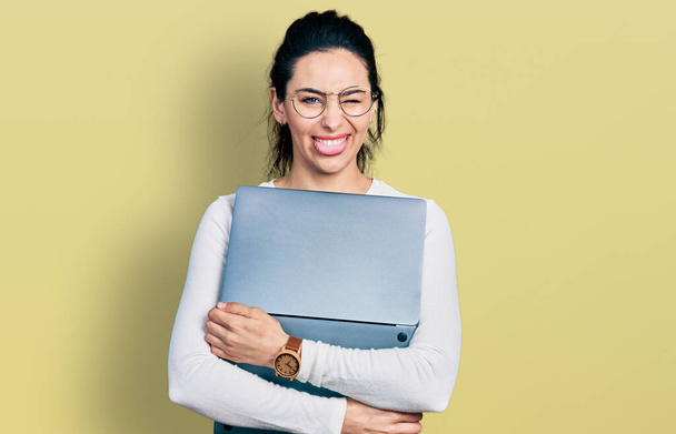 Mujer hispana joven trabajando usando computadora portátil sacando la lengua feliz con expresión divertida.  - Foto, Imagen