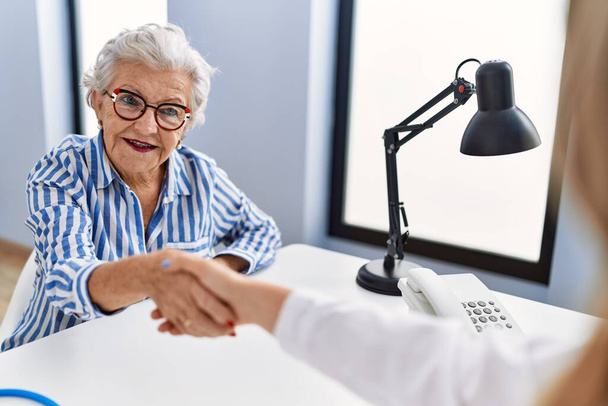 Senior grey-haired woman patient having medical consultation shake hands at clinic - Valokuva, kuva