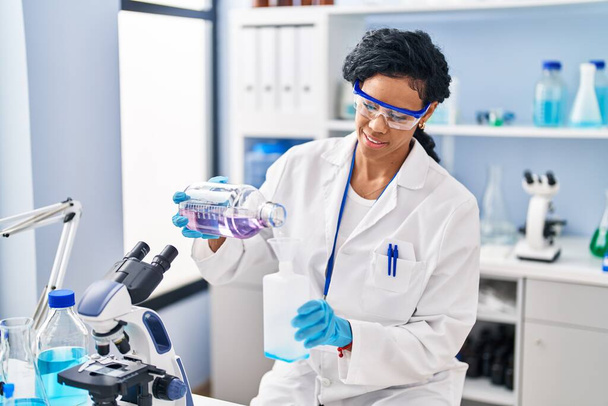 African american woman wearing scientist uniform measuring liquid at laboratory - 写真・画像