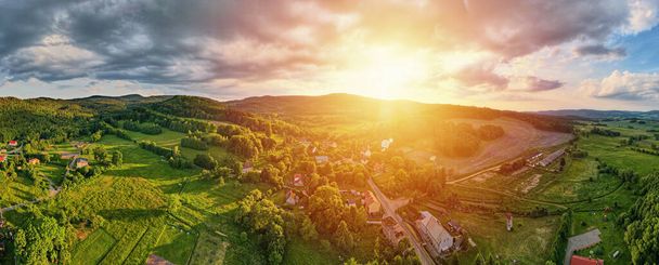 Vista aerea di un bellissimo paesaggio al tramonto, vista aerea della zona di campagna con villaggio e campi verdi vicino alle montagne, lungo panorama - Foto, immagini