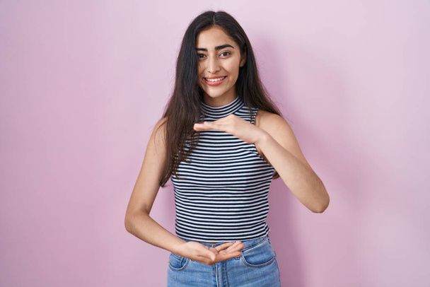 Mladá dospívající dívka v neformální pruhované tričko gestikulující s rukama ukazujícími velkou a velkou značku velikosti, symbol míry. s úsměvem na kameru. koncepce měření.  - Fotografie, Obrázek