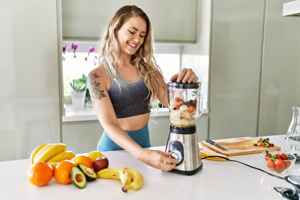 Young woman smiling confident blending healthy smoothie at kitchen - Photo, Image