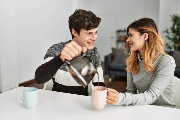 Young caucasian couple having breakfast pouring coffee on cup at home. - Fotó, kép