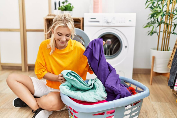 jong blond meisje doen wasgoed zetten kleding in wasmachine thuis. - Foto, afbeelding