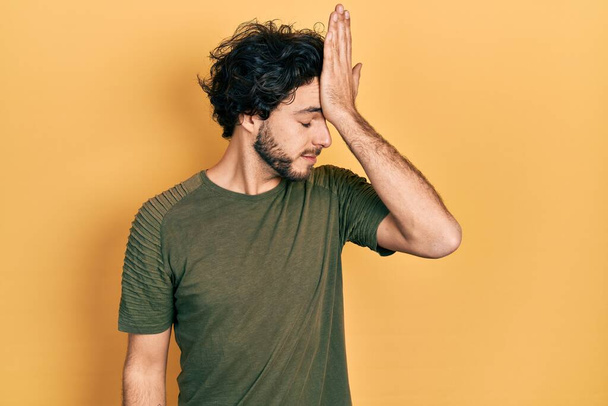 Schöner hispanischer Mann in lässigem grünem T-Shirt überrascht mit der Hand auf dem Kopf für Fehler, erinnere dich an Fehler. Vergessenes, schlechtes Gedächtnis.  - Foto, Bild