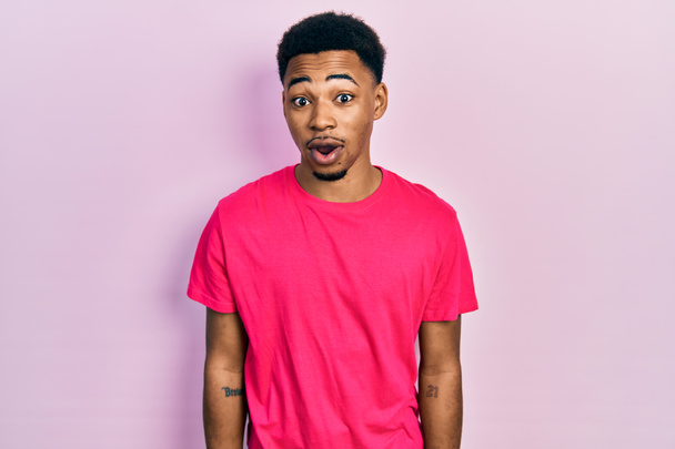 Fiatal afro-amerikai férfi visel casua póló fél, és megdöbbent a meglepetés kifejezés, félelem és izgatott arc.  - Fotó, kép