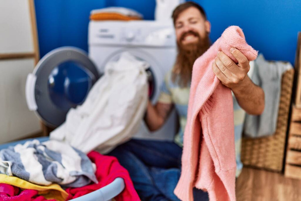 若い赤毛の男は洗濯室で自信を持って洗濯服を笑って - 写真・画像