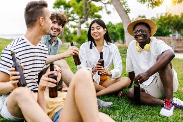 Молода група кращих друзів, що висять у міському парку, п "ючи пиво, зосереджується на африканському чоловікові, який дивиться на камеру. - Фото, зображення